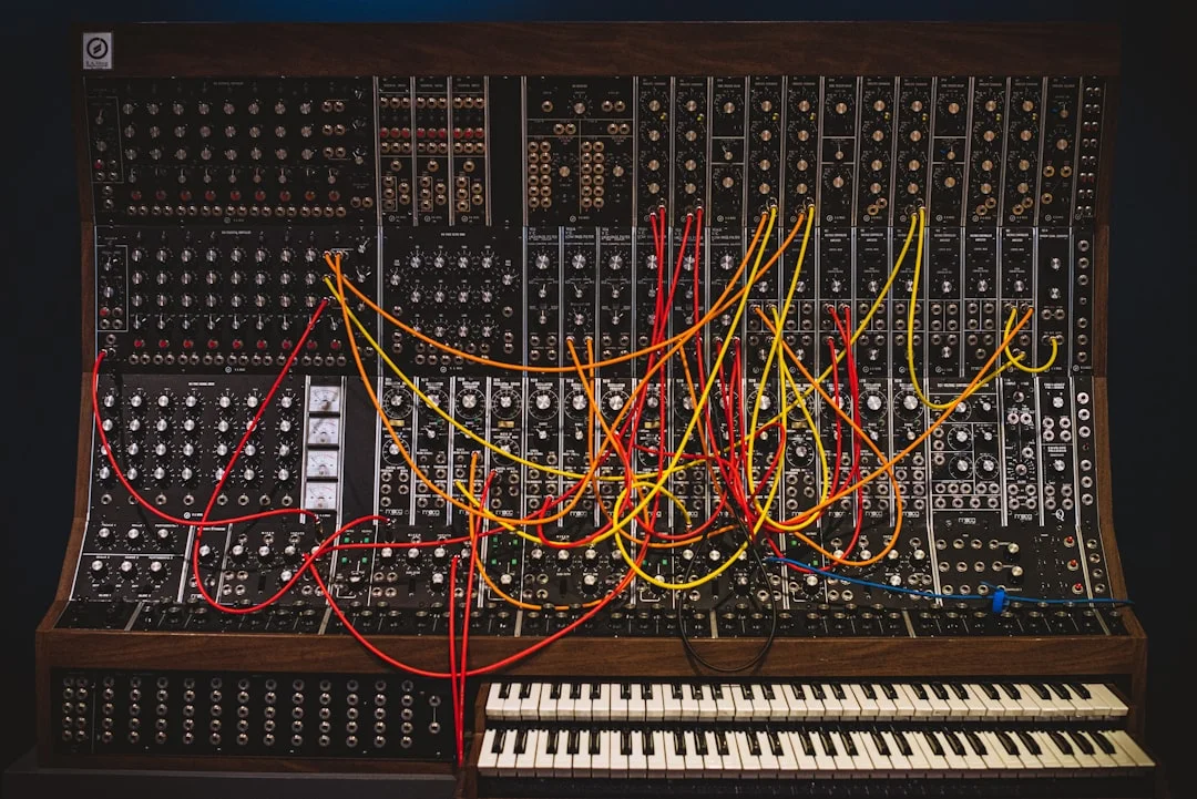 A dimly lit studio desk with an Elektron Analog Rytm MKII center stage, surrounded by Eurorack modules, patch cables, and a glowing sequencer grid reflecting off the surface